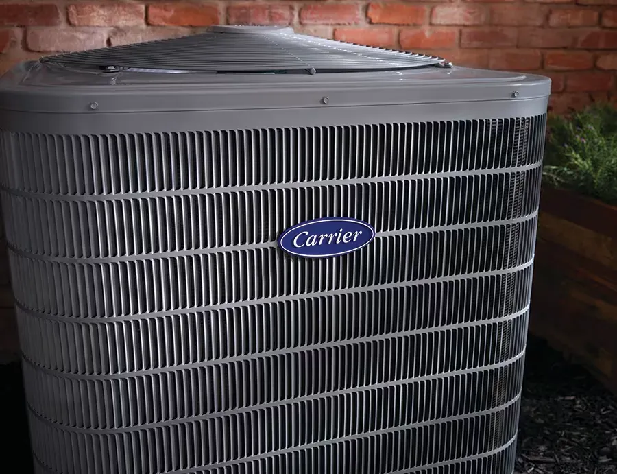 A carrier air conditioner is sitting in front of a brick wall A carrier air conditioner is sitting in front of a brick wall
