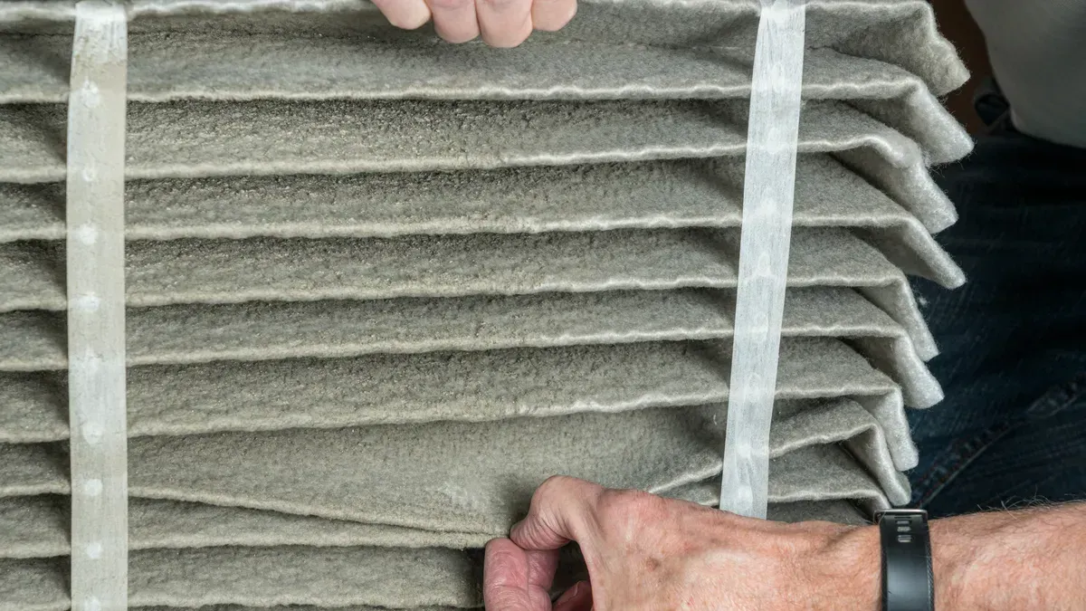A person is holding a dirty air filter in their hands.