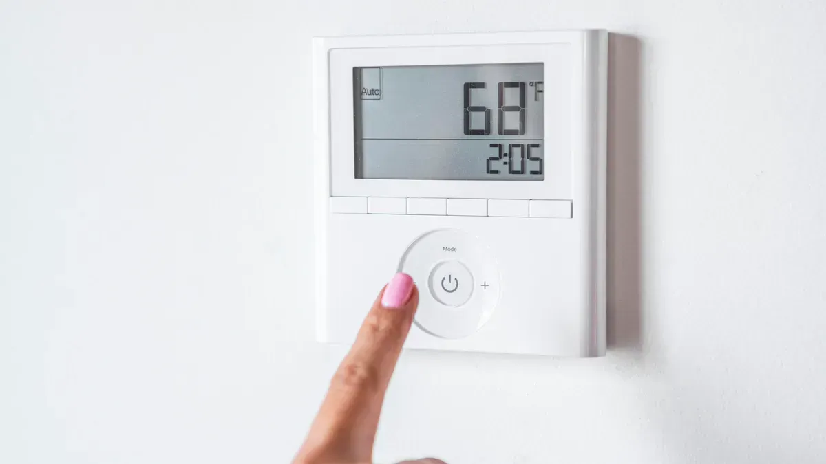 A woman is adjusting the temperature on a thermostat. A woman is adjusting the temperature on a thermostat.
