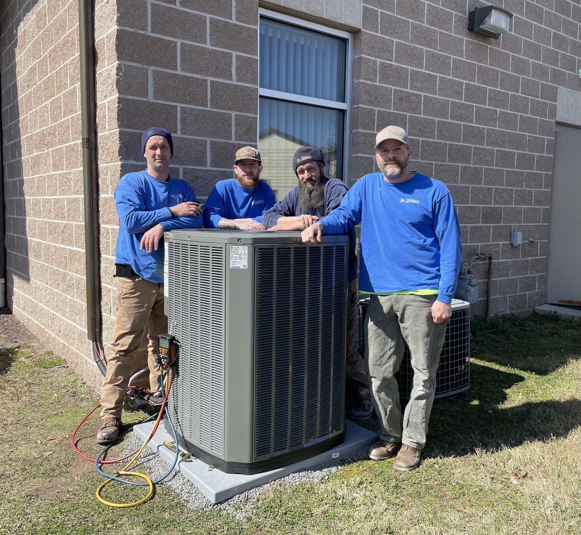 Three men from Nauman Inc. are standing next to a large air conditioner.