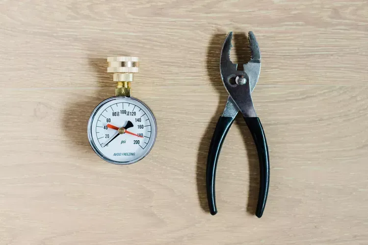 A pressure gauge and pliers are sitting on a wooden table. A pressure gauge and pliers are sitting on a wooden table.