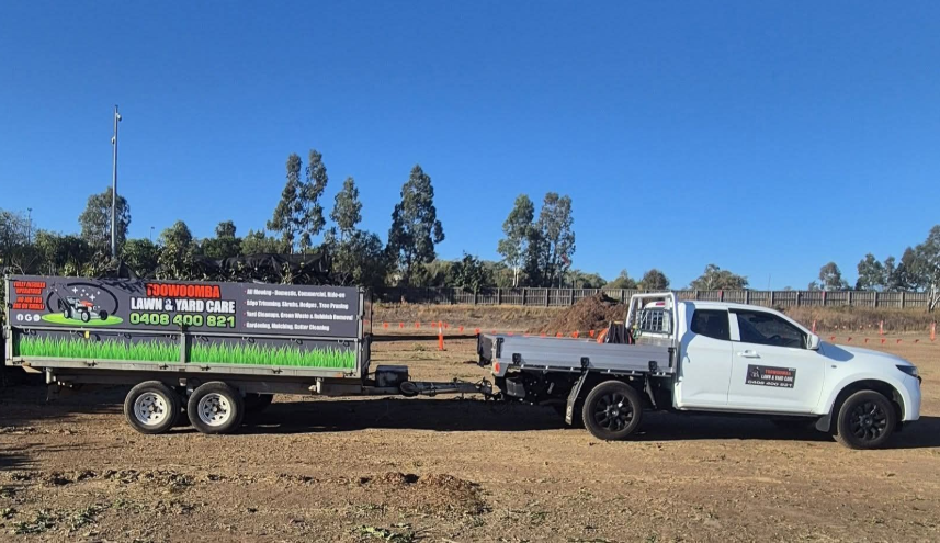 White pickup truck towing a sign-covered trailer on a dirt road under a clear blue sky— Toowoomba Lawn and Yard care In Glenvale, QLD