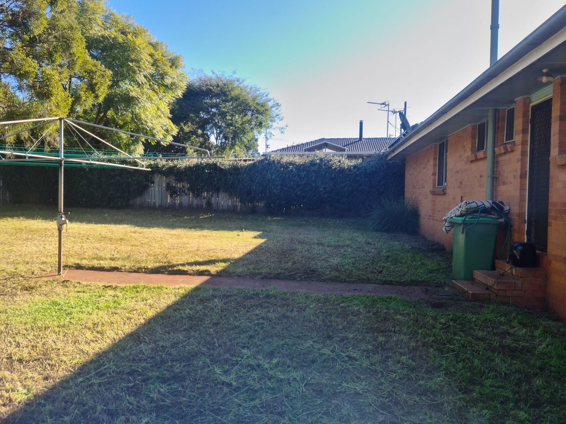 Backyard With Grass, Clothesline, Brick House, and a Green Trash Bin — Toowoomba Lawn and Yard care In Glenvale, QLD