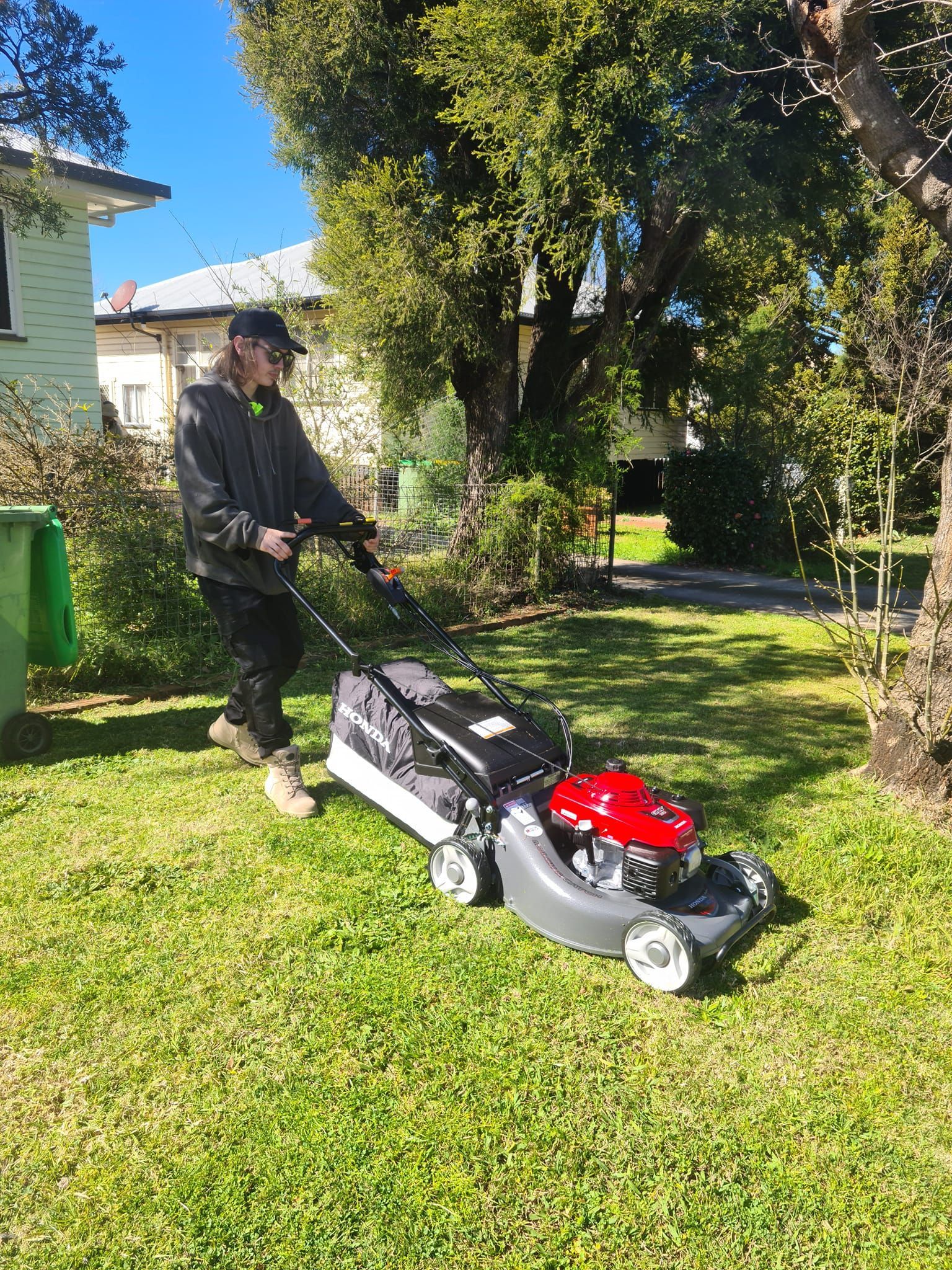 Person Pushing a Red-and-gray Lawn Mower Across a Grassy Yard — Toowoomba Lawn and Yard care In Westbrook, QLD