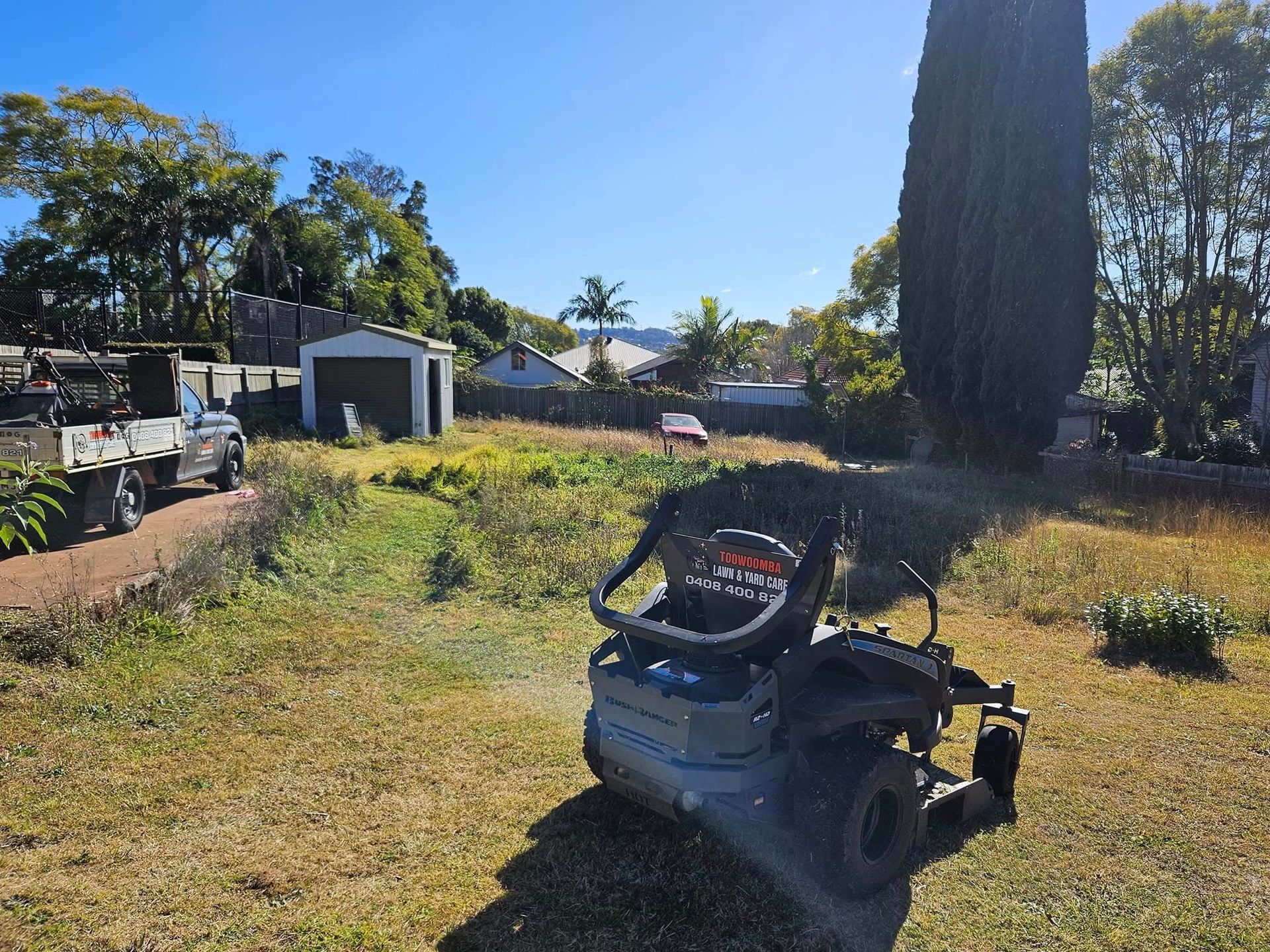 A Riding Lawn Mower on a Sunlit Grassy Yard With Trees — Toowoomba Lawn and Yard care In Westbrook, QLD