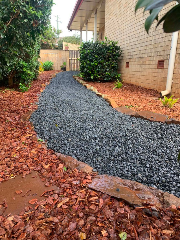 Narrow dark gravel path beside a brick house, bordered by reddish mulch and shrubs— Toowoomba Lawn and Yard care In Glenvale, QLD