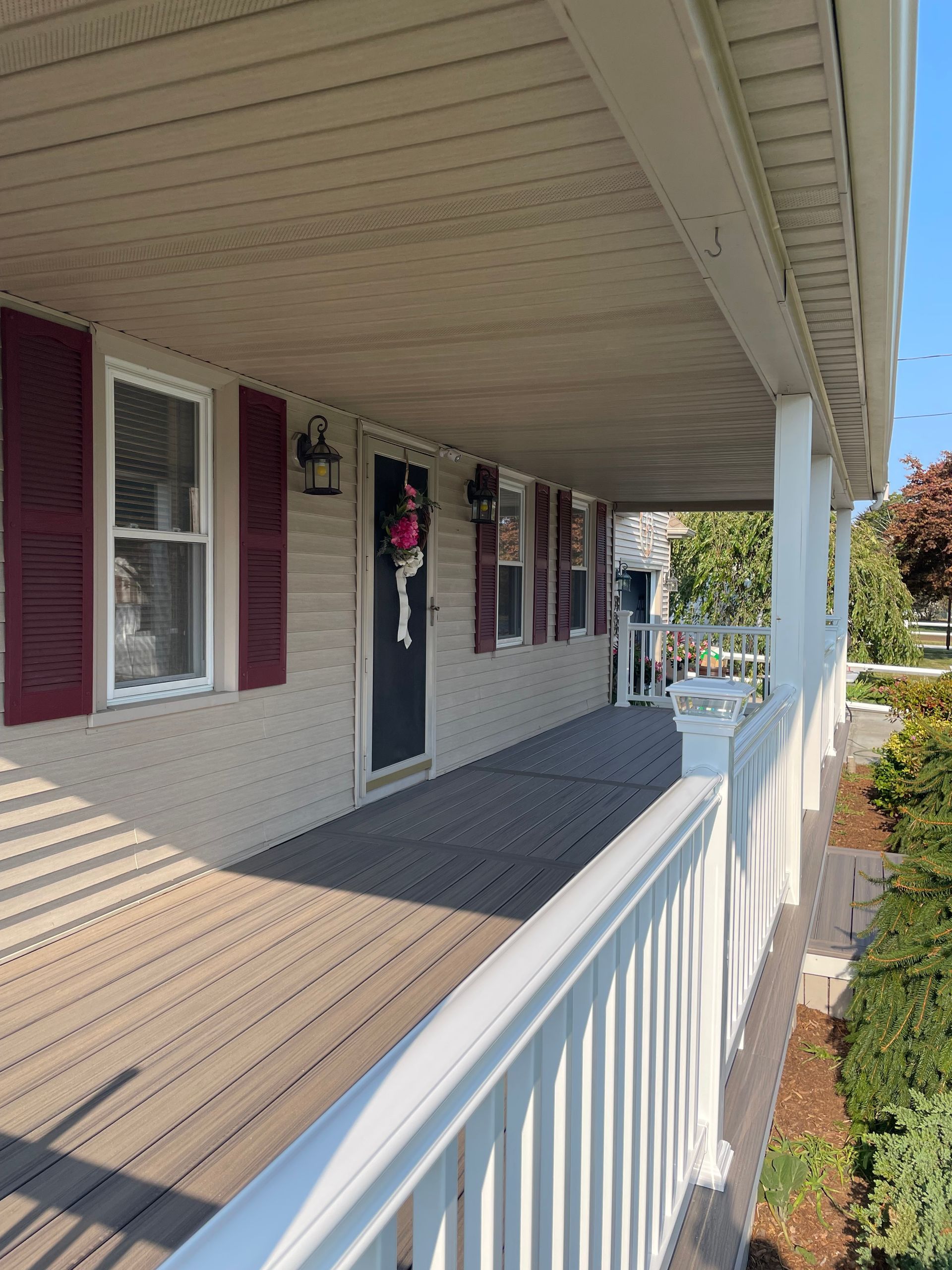 The porch of a house with red shutters and a white railing.