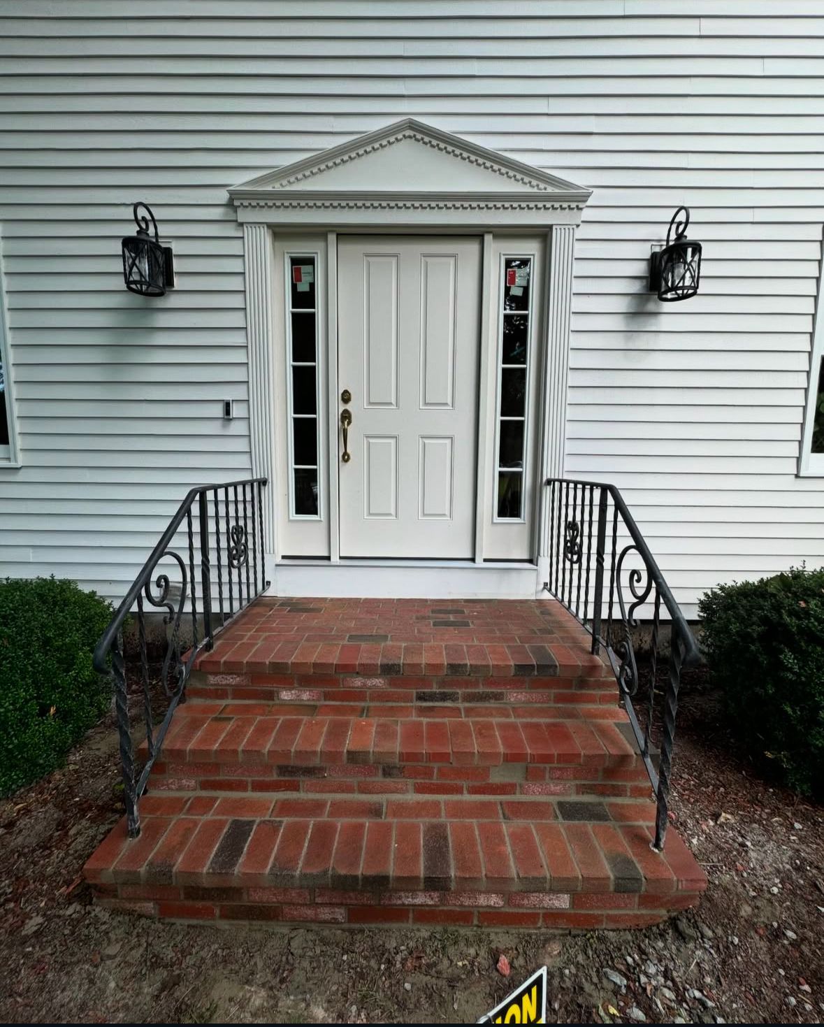 The front door of a white house with brick steps and a wrought iron railing.