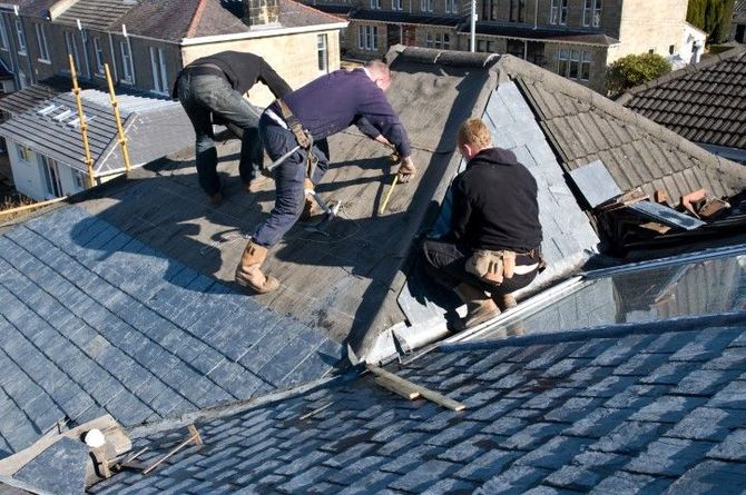 Roofers repairing a blue-tiled roof, working around a damaged section near the ridge