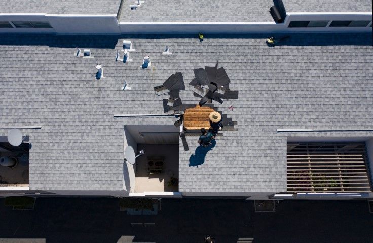 Overhead view of a rooftop with two people near an open hatch and a ladder shadow