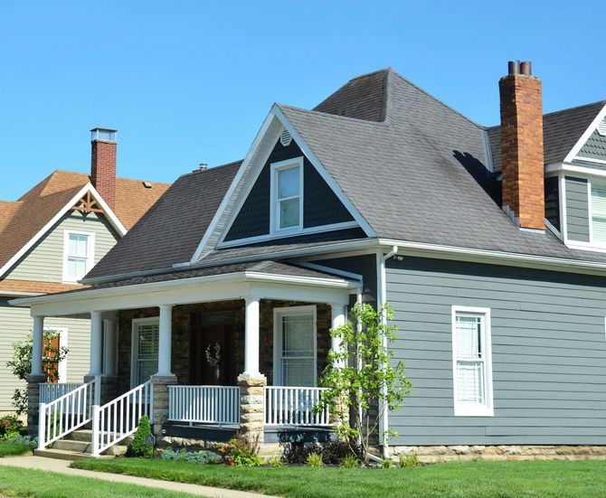 Gray house with a front porch and white trim on a sunny residential street