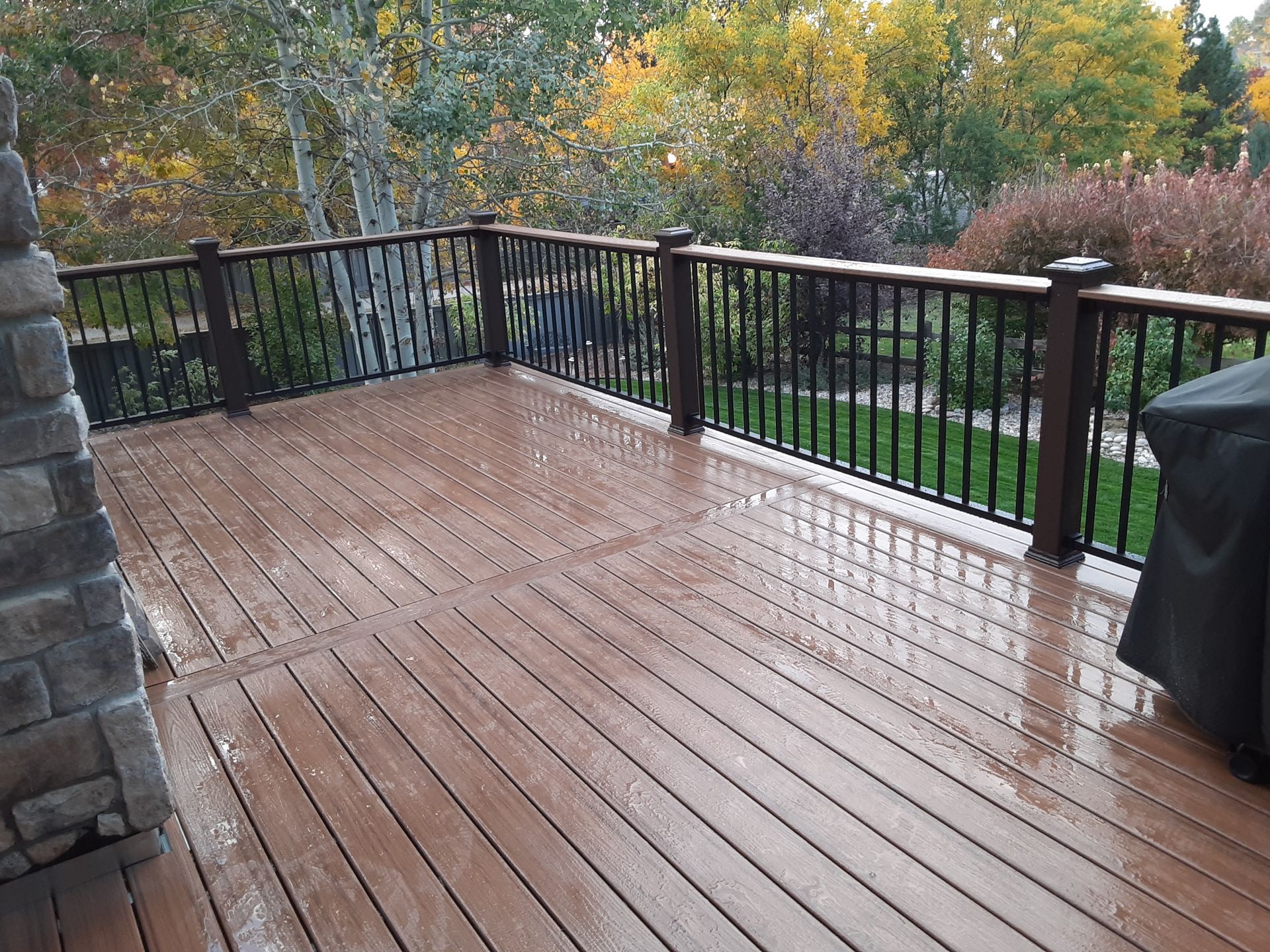 A wooden deck with a metal railing and a grill on it.