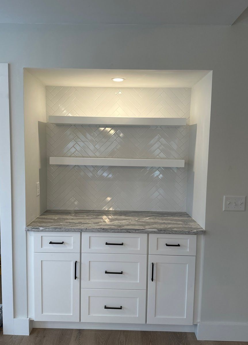 A kitchen with white cabinets , drawers , and a marble counter top.