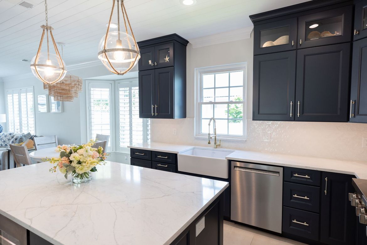 A kitchen with black cabinets , white counter tops , stainless steel appliances and a large island.