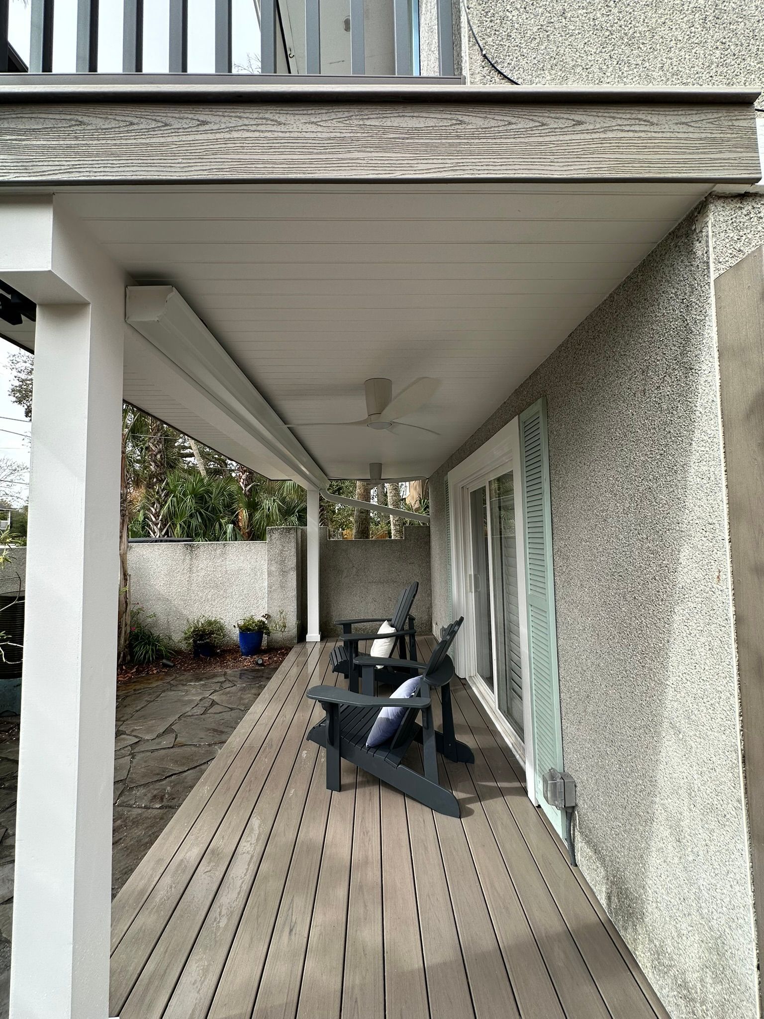 A wooden deck with chairs and a ceiling fan on the side of a house.