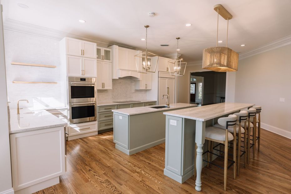 A kitchen with white cabinets , stainless steel appliances , hardwood floors and a large island.