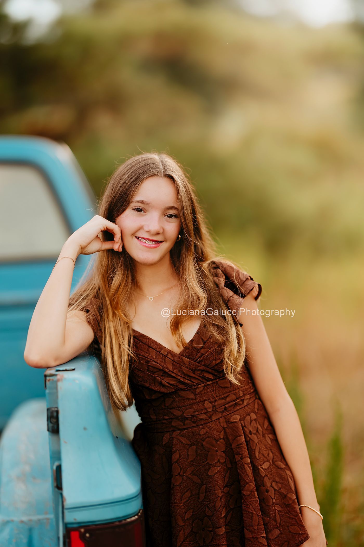 Teenager girl Smiling beside a vintage blue truck at a private farm during a Raleigh Portrait session.