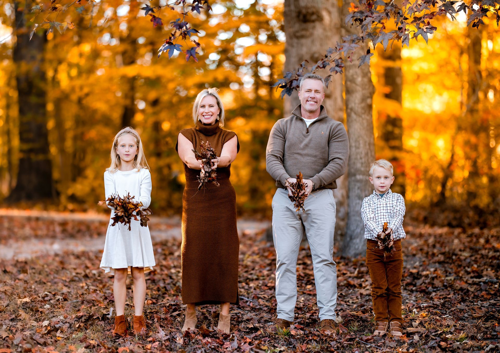 Family smiling and posing among colorful fall leaves during a golden hour fall family photography session in Raleigh, NC.