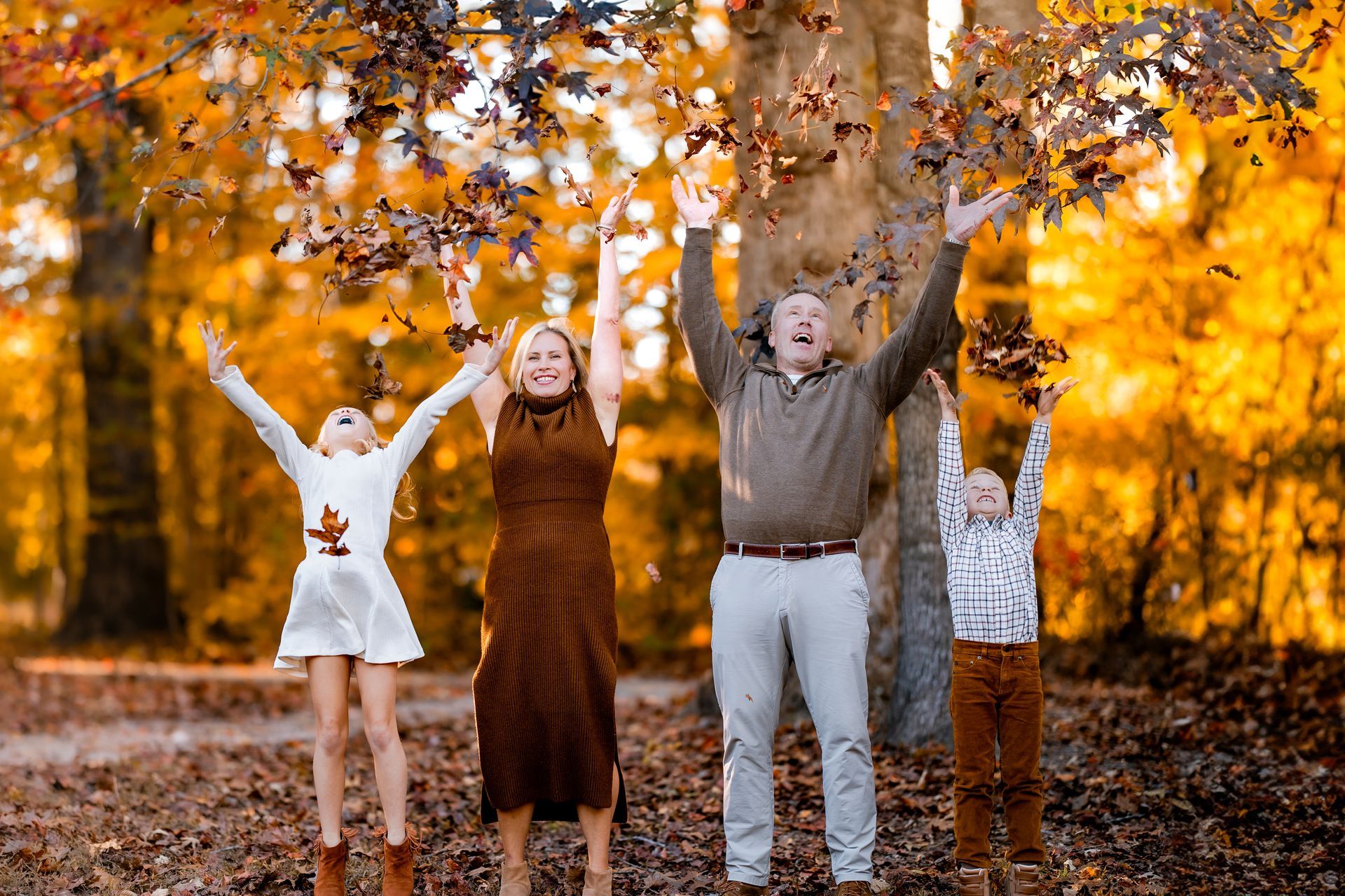 Family throwing colorful fall leaves in the air during a golden hour fall family photography session in Raleigh, NC.