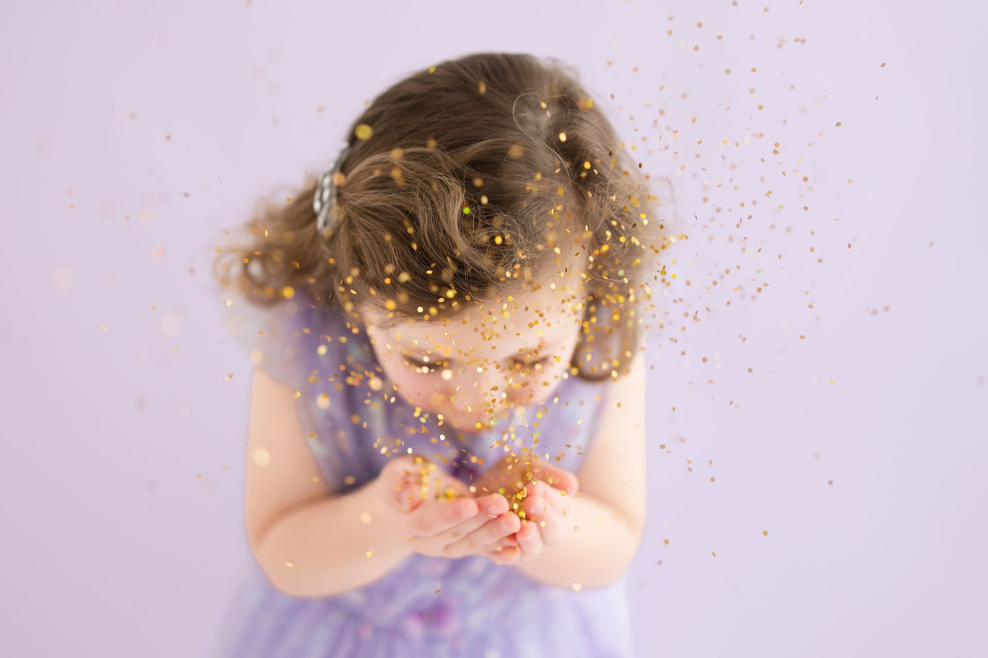 4-year-old girl blowing purple glitter during magical studio birthday session