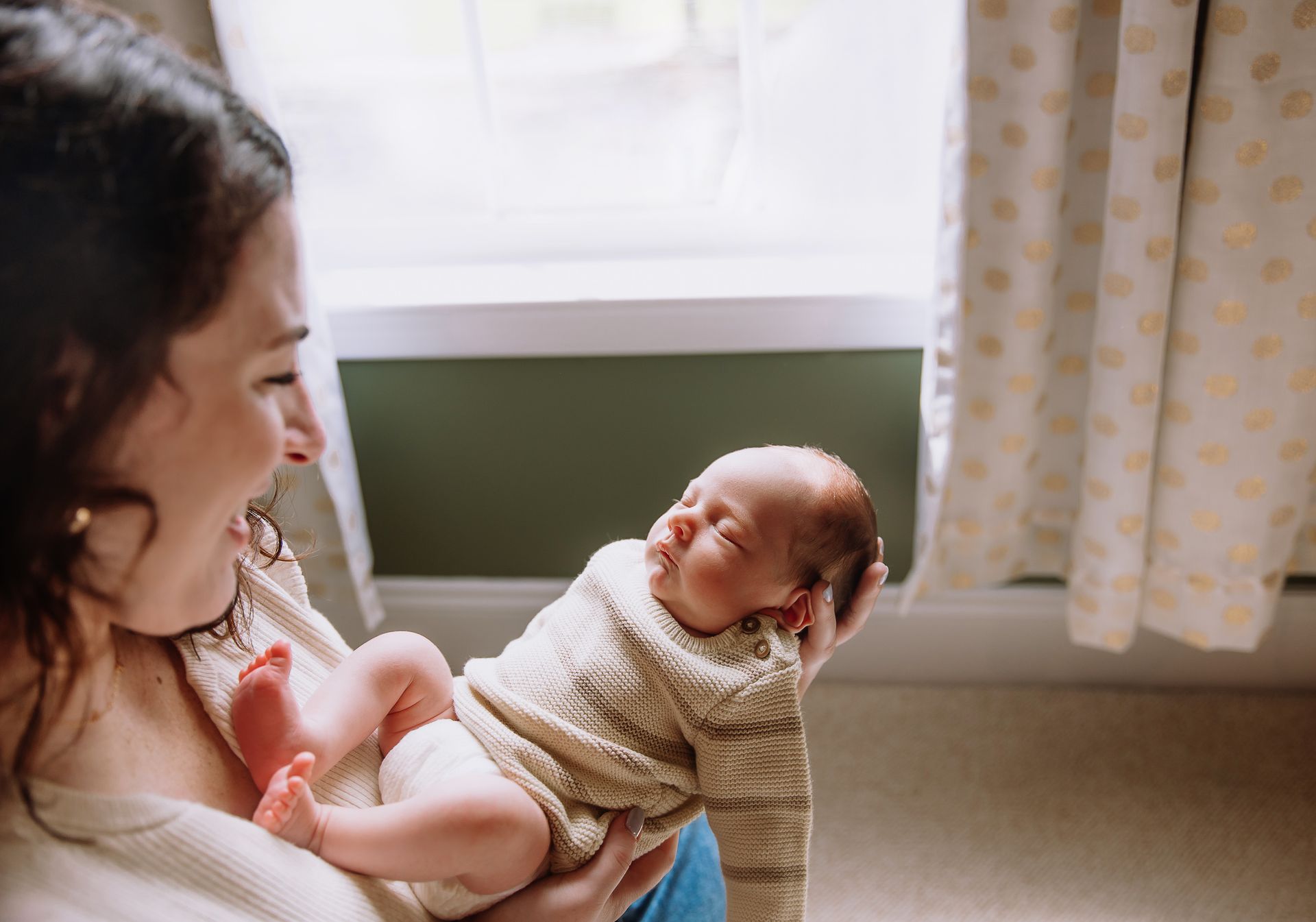 Mother holding newborn near window during lifestyle newborn session in Raleigh