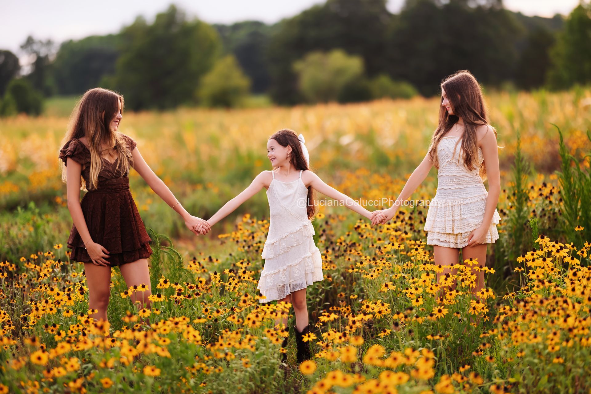 Sisters smiling among blooming wildflowers during a sunset family session.