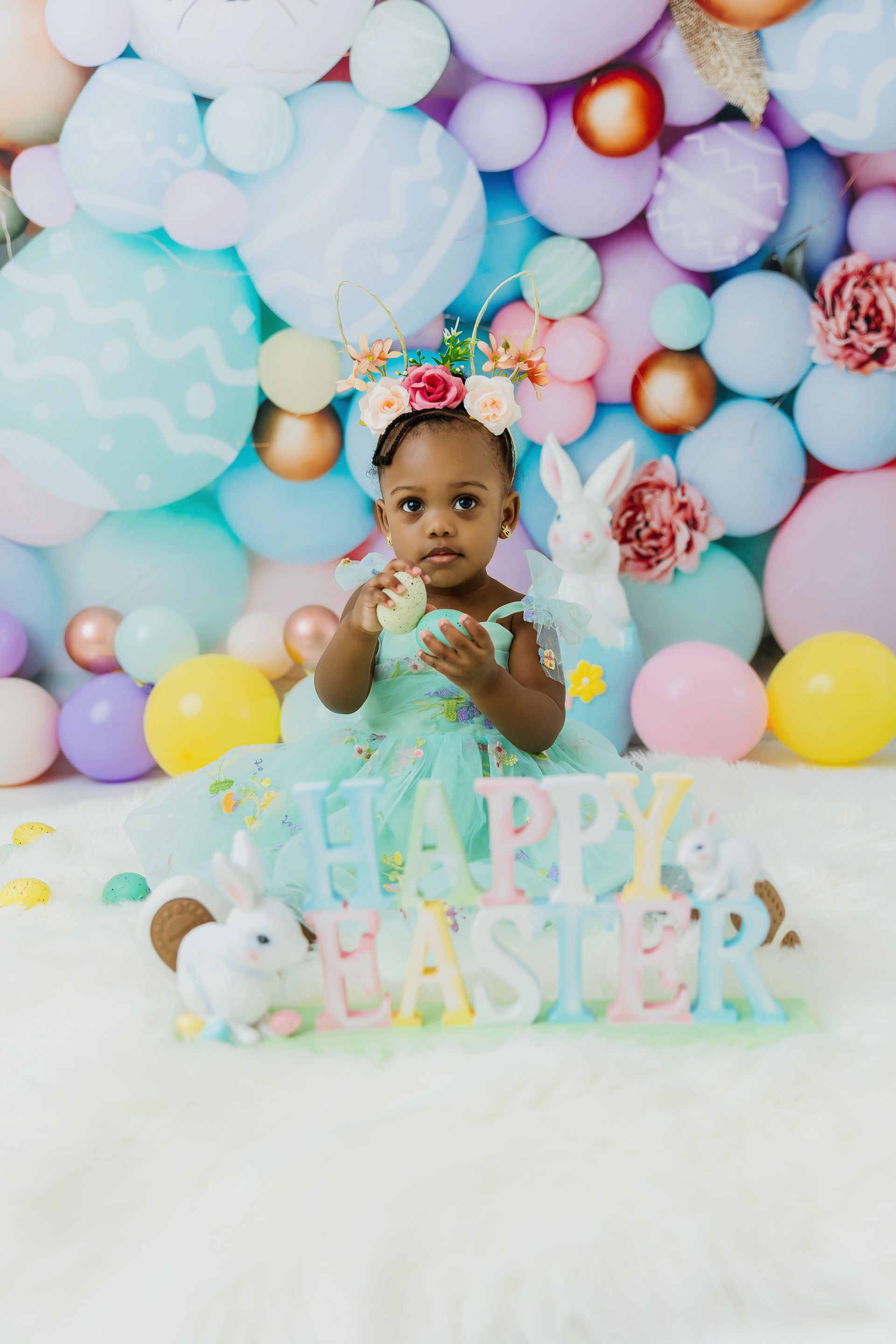 Easter mini session with a toddler girl posing next to a happy easter sign in Cary NC photography studio