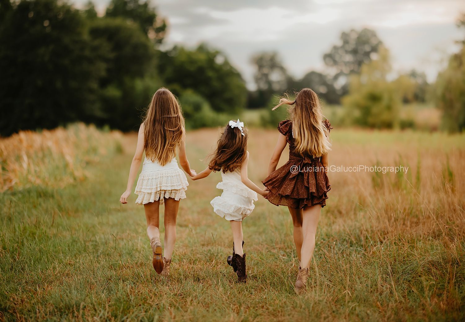 Three sisters skipping through golden grass at sunset during a Raleigh sibling photo session.