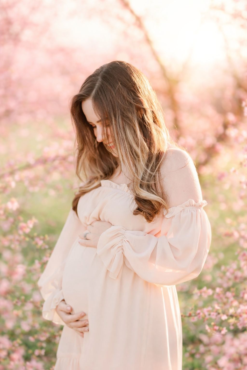 Expecting mother holding baby bump surrounded by peach blossoms during maternity photos in Raleigh NC