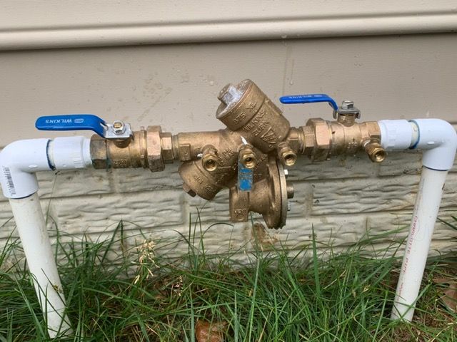 A water valve with a blue handle is attached to a pipe in the grass.