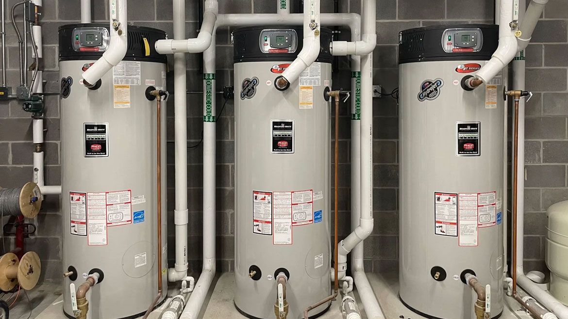 Three water heaters are lined up next to each other in a room.