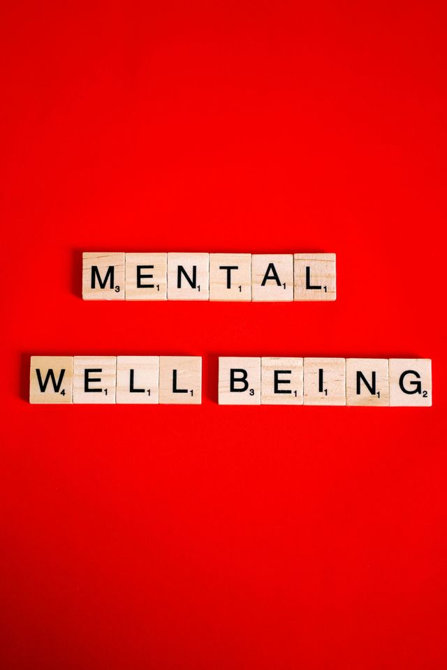 The words mental well being are written in scrabble tiles on a red background.