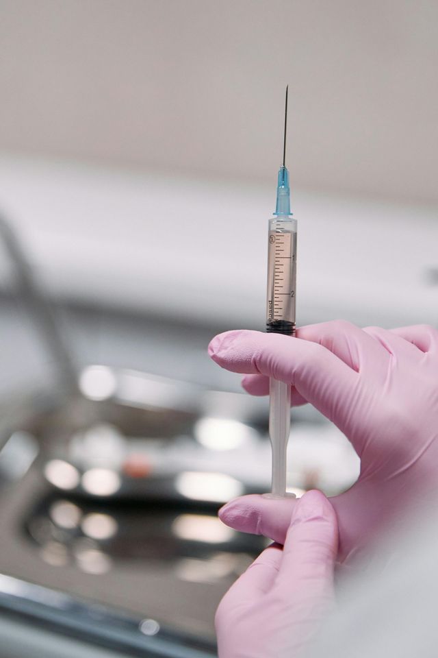A person wearing pink gloves is holding a syringe.