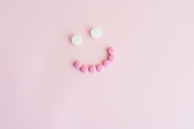 A smiley face made of pink and white pills on a pink background.
