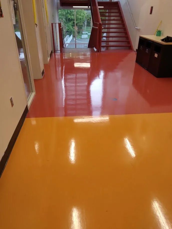 A hallway with a red floor and stairs in the background.