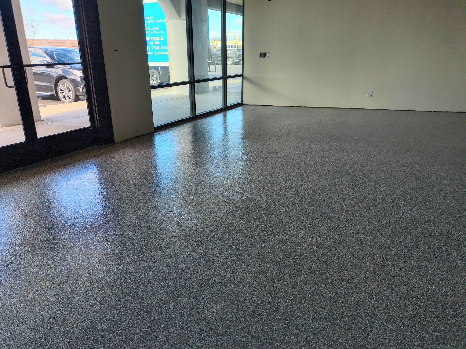 Empty retail space with gray speckled epoxy floor and large front windows and glass doors