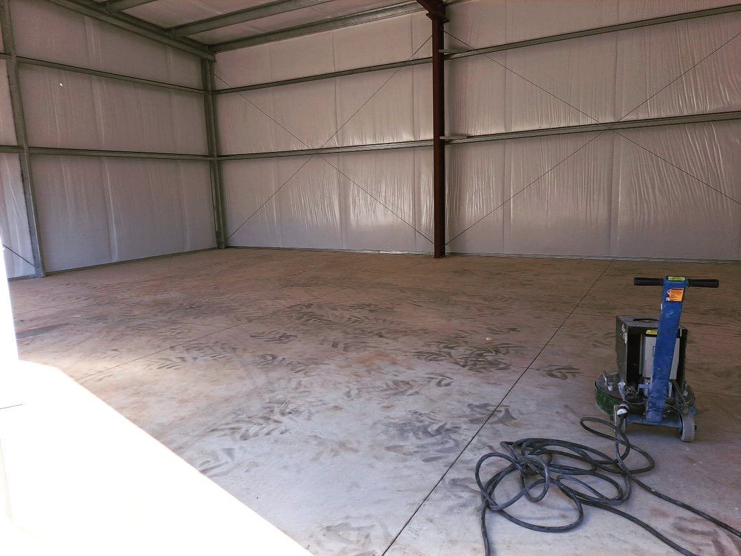 Empty metal warehouse interior with concrete floor and a blue hand truck in the right foreground