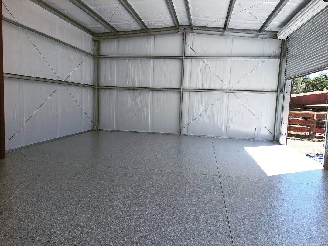 Empty metal warehouse interior with white walls and a gray speckled floor, lit by sunlight from the open door