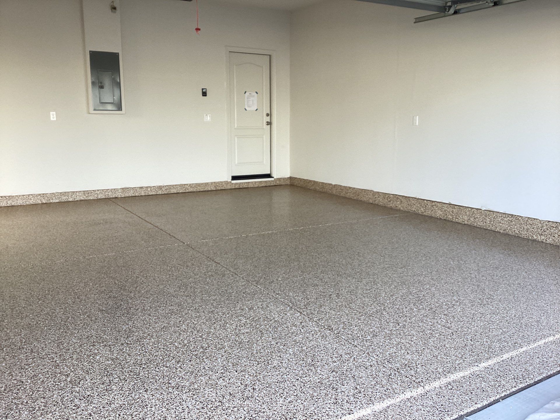 Empty garage with speckled epoxy floor, white walls, and a side door.