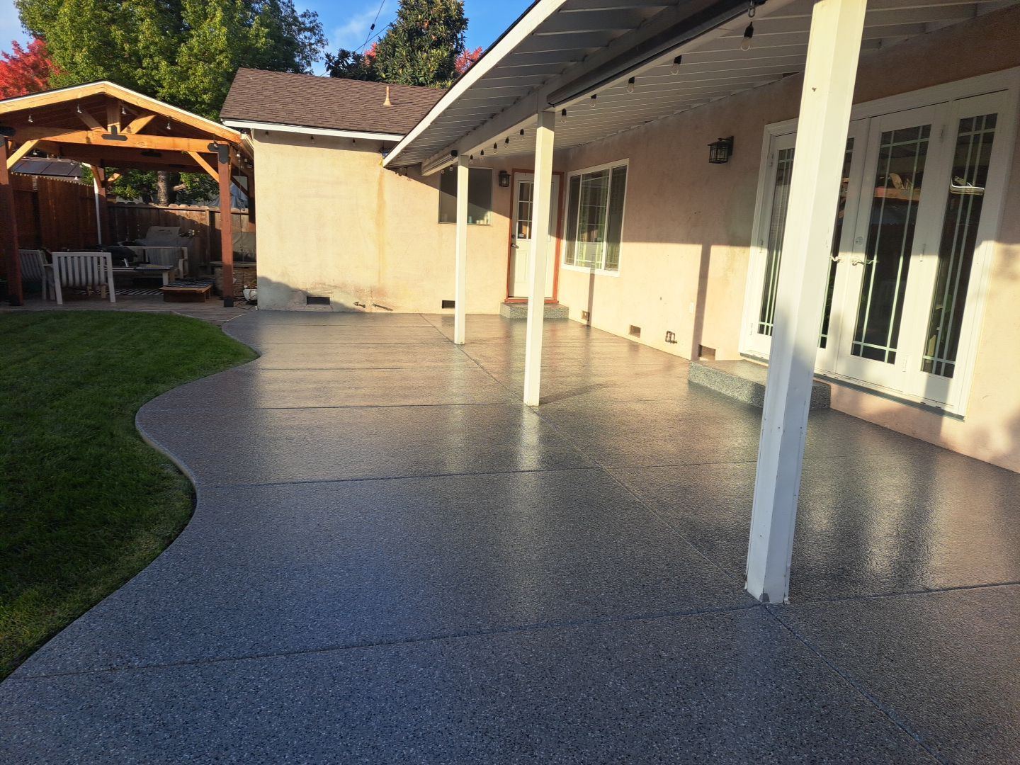 Covered patio with white columns and speckled concrete floor beside a house and lawn