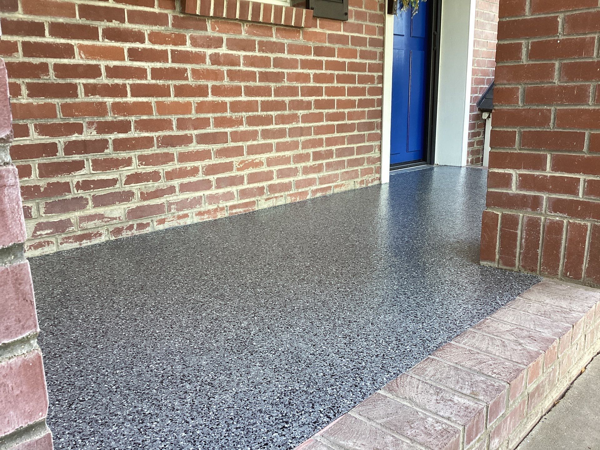 Brick building entrance with blue door and speckled gray ramp leading up from the sidewalk