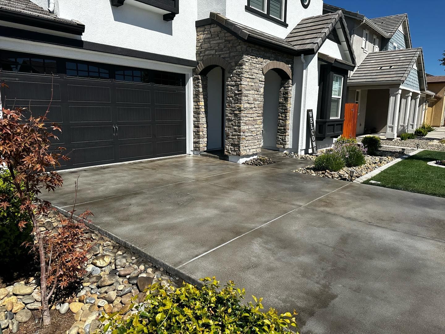 Suburban house exterior with black garage doors, stone facade, and a concrete driveway in bright sunlight