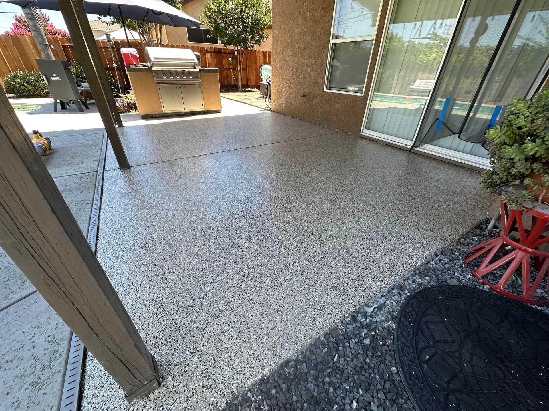 Patio with speckled concrete floor, sliding glass door, and outdoor seating area in sunlight