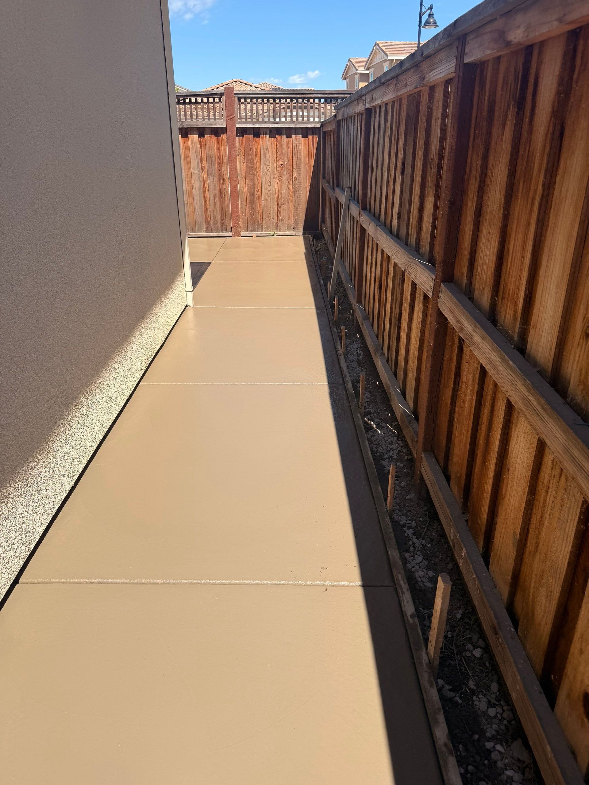 Narrow concrete side yard with a wooden fence and gate in bright sunlight