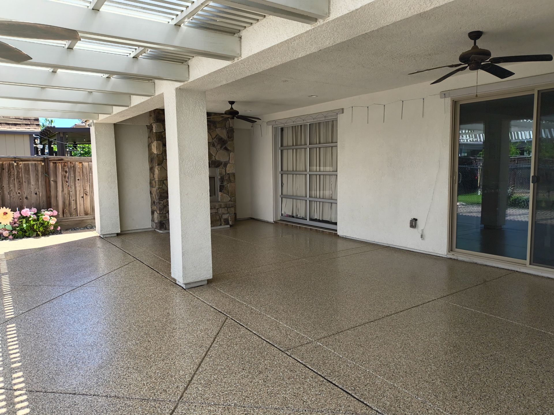 Covered patio coated concrete with white columns, tiled floor, ceiling fan, and sliding glass doors.