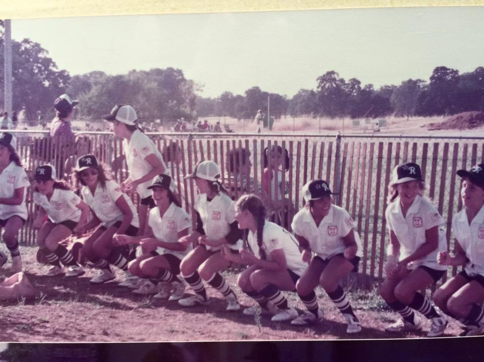 Group of people in white shirts and hats posing outdoors by a fence on a sunny day