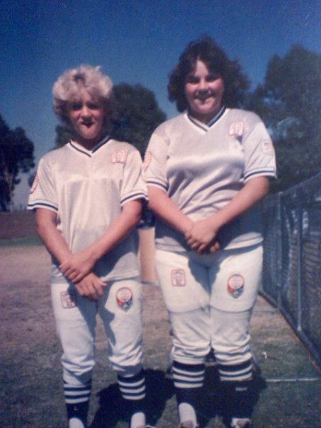 Two soccer players in white uniforms standing side by side on a grassy field, smiling outdoors.