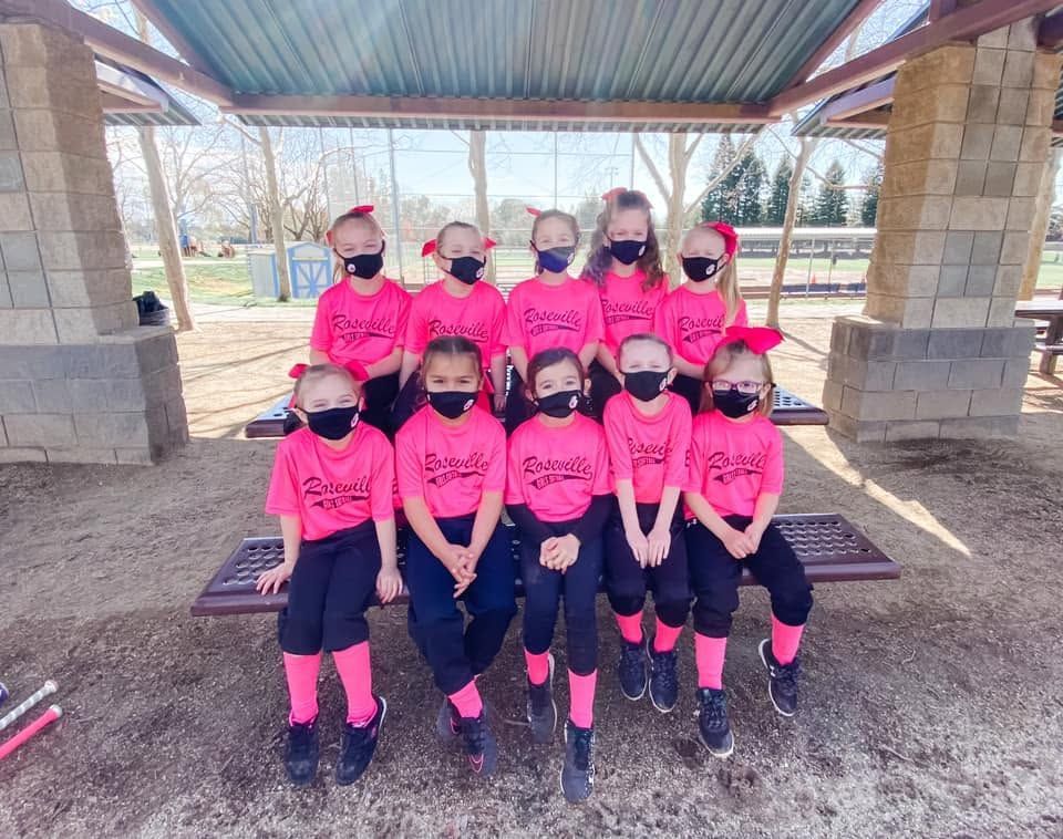 Youth sports team in bright pink shirts and black masks posing under a pavilion on a bench