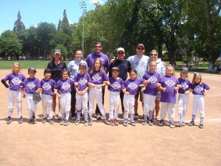 Youth baseball team in purple uniforms posing with coaches on a sunny field.