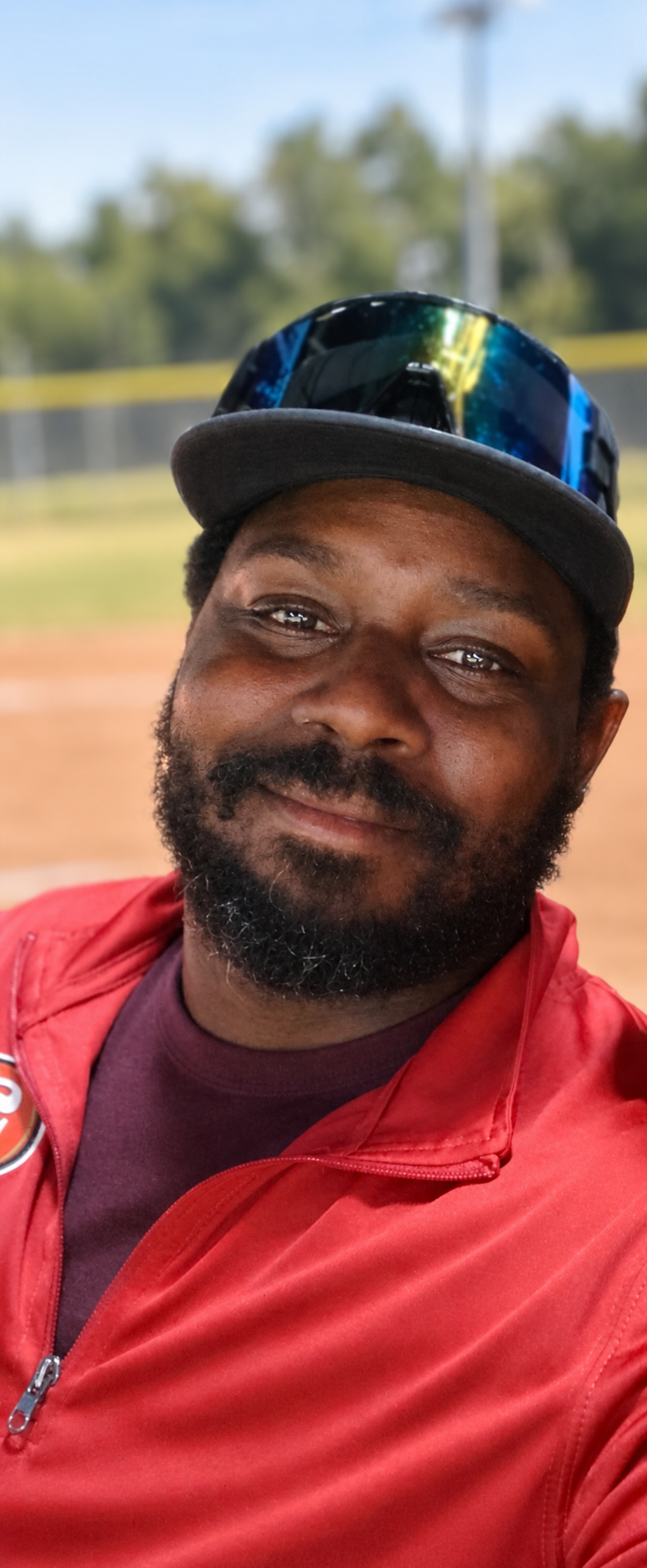 Smiling man in a red shirt and blue cap outdoors on a sunny field